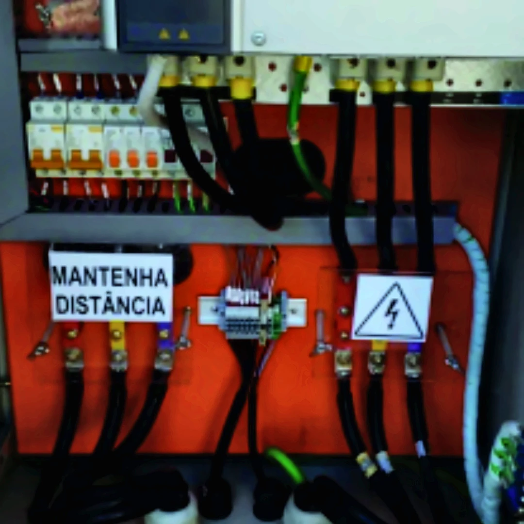 Interior de painel elétrico com componentes, cabos e sinalização de segurança